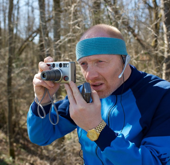 Mann mit türkisem Stirnband blickt angestrengt auf das Display einer digital Kamera