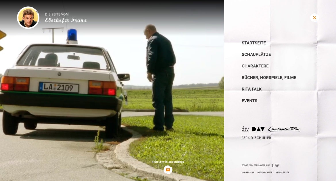 Ein Auto mit blaulicht auf dem Dacht steht am Straßenrand, daneben steht ein Mann in dunkler Kleidung und blickt hinein.